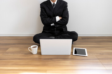 床に座ってノートパソコンを操作しているスーツ姿の男性