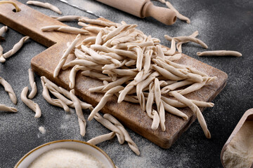 Whole grain wheat apulian pasta called Pizzarieddi or maccaruni on a cutting board on black table. Fresh maccheroni typical dish of Puglia, Salento Italy. Italian homemade pasta background, close up
