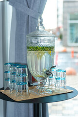  water in glassware in the form of a samovar near the window on the table. Lemon slices and mint leaves float in it. 