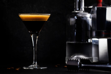 Espresso martini cocktail with vodka, coffee liqueur, syrup and ice, dark bar counter background, bar tools, copy space