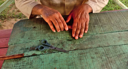 Hands of elderly man working rolling cigars on green and old table