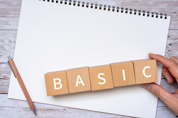 「BASIC」と書かれた積み木とペン、ノート、人の手