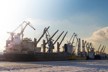 Fototapeta na wymiar Shipyards on the bay in winter. Cranes, trawlers and ships at sunset on a frosty day.