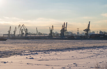 Obraz premium Shipyards on the bay in winter. Cranes, trawlers and ships at sunset on a frosty day.