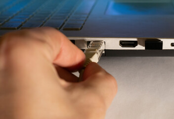 A hand holds an internet cable to connect a home network. LAN cable connection with laptop.