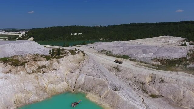Loaded truck moving along the road at present day kaolin mine. White hilly ground, blue water and clear sky. Green trees at the backdrop.