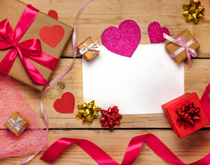 Top view photo of Valentine's day decor gift box, paper heart, a sheet of paper on a wooden background.
