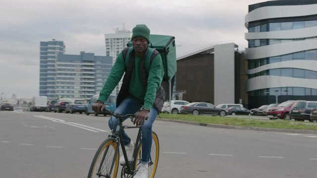 A young black delivery man with a backpack carries an order on a bicycle