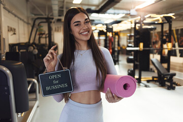 A beautiful young girl, looking at the camera with a smile on her face, holds a sign that the gym...