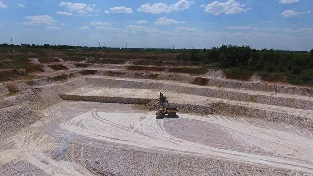 Straight ground at the kaolin quarry. Excavator machine digging the rock formations. Lorry approaching to be uploaded with minerals.