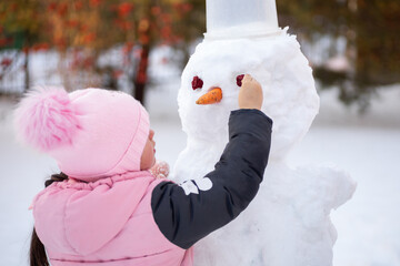 Young girl alone making face of snowman with improvised means in daytime while having walk in park...