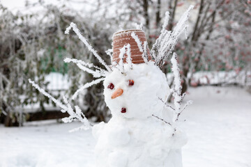 Closeup of head of hand made snow man on backyard with carrot nose, cone eyes, flower pot on head and tree twigs instead of hands and hair. Spending snowy winter time together as family. 