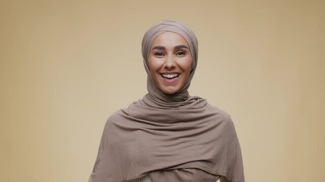 Greeting concept. Young positive talkative middle eastern lady wearing hijab waving hand to camera and smiling