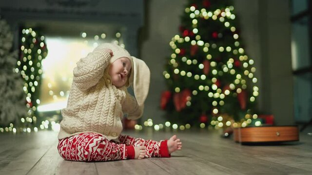 Baby in rabbit costume pulls his ears. Family Spending Winter Evening at Home. Young Mother with Little Kid Son play. Slow Motion. Christmas, New Year, Winter Holiday Celebration. 4K 10 bit colors