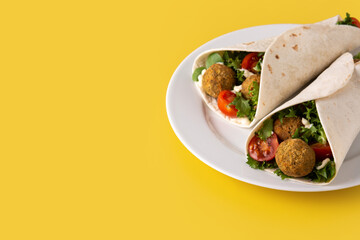 Tortilla wrap with falafel and vegetables on yellow background. Copy space