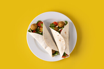 Tortilla wrap with falafel and vegetables on yellow background