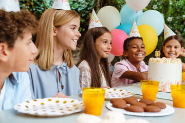 Multiracial children in party cones smiling during birthday party