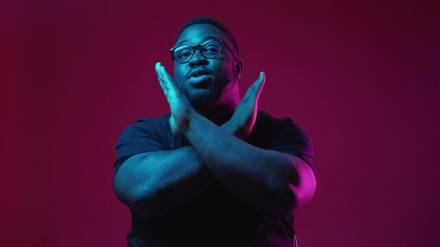 No gesture. Refusing man. Stop rejection. Serious displeased guy showing denial expression in vibrant neon light on burgundy background.
