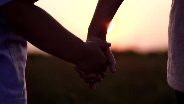 Happy Family Concept. Close-up two little sisters hands joining and holding hand together run across the field with sunset sunlight flare in beautiful natural background, Slow motion.