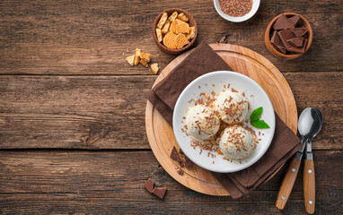 Three balls of creamy ice cream with chocolate chips on a wooden background.