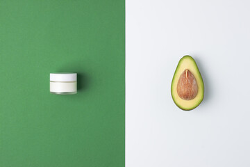 Minimal composition with jar of cosmetic cream and avocado on green and white background. Flat lay, copy space