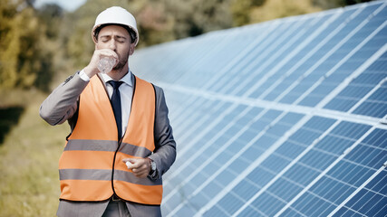 businessman in safety vest drinking water near solar panels