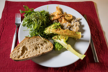A dinner plate with broccoli, risotto, shrimp , salad and bread.