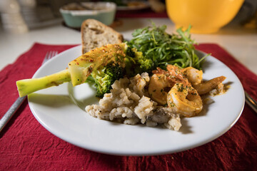 A dinner plate with broccoli, risotto, shrimp , salad and bread.