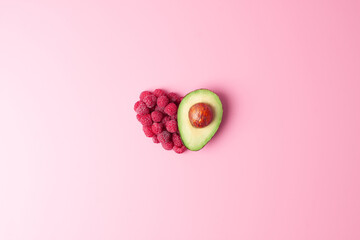 Creative summer concept. Heart shape made from fresh berries and avocado on pink background. Flat...