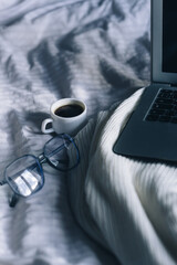 a cup of coffee, laptop glasses on the background of a white bed and a light plaid. relaxation and comfort. work from home. sickness work in bed