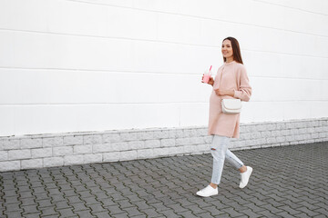 Beautiful young pregnant woman wearing pink sweater, jeans and white sneakers walking through the...