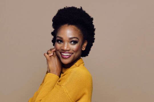 Young Adult Black Woman Smiling With Hand On Chin Wearing Yellow Sweater Close Up