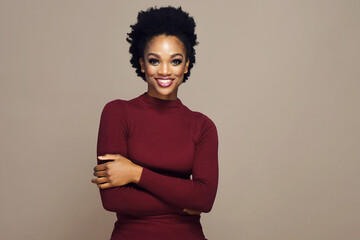 Portrait of happy smiling beautiful young woman with arms crossed curly hair wearing red sweater against gray background