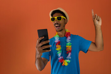 Black man in costume for brazil carnival holding mobile isolated on orange background. African man in various poses and expressions.