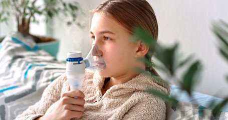 Teenage girl makes inhalation with a nebulizer equipment. Sick child holding inhalator in hand and...