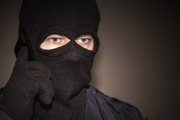 An extortionist in black clothes with a balaclava covering his face. A cruel fraudster uses a...
