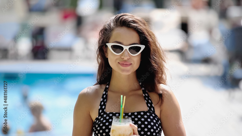 Wall mural happy young woman in sunglasses and swimsuit holding cocktail in glass