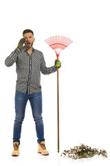 Shouting gardener is standing with a leaf rake. Full length studio shot.