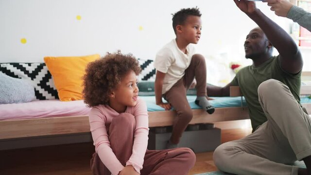 Two little multiracial kids with mother and father playing with toy planes at home.