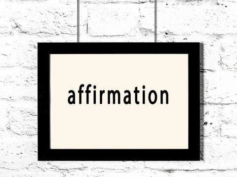 Black frame hanging on white brick wall with inscription affirmation
