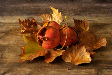 Naklejka na ściany i meble Horizontal shot of some pomegranates on top of autumn leaves on a wooden table.