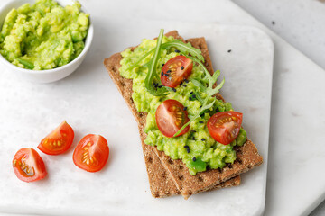 Healthy breakfast wholewheat toast with avocado slices, tomatoes and black sesame seeds on board.