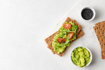 Tasty avocado toasts with  tomatoes cherry and black sesame seeds on white board. Top view. Copy space