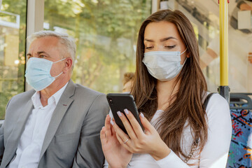Beautiful brunette woman holds phone in hand browsing social media student on way back from university by bus on face is protective mask required for public transportation elderly man sit next to girl