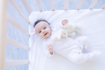 baby girl smiling on the bed on a white cotton bed with a toy falling asleep or waking up in the morning, cute newborn little baby at home in the crib