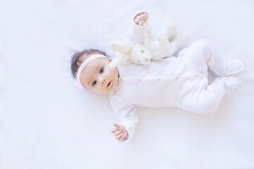 baby girl smiling on the bed on a white cotton bed with a toy falling asleep or waking up in the morning, cute newborn little baby at home on an isolated background close-up