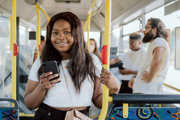 A dark-skinned woman rides in a public transport bus holding on to a barrier, a girl buys an...