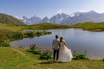Bride and groom getting married at the Koruldi Lake with a dream like view on mountains near Mestia in the Greater Caucasus, Upper Svaneti, Country of Georgia. Horses at the water shore. Fairytale