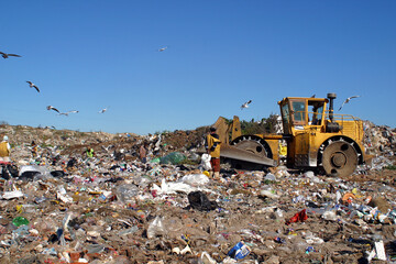 A bulldozer working at a landfill site, with laborers picking waste for recycling.