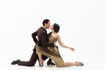 Handsome man in classic brown suit and woman in elegant gold dress standing on their knees in dance movement looking eye to eye.